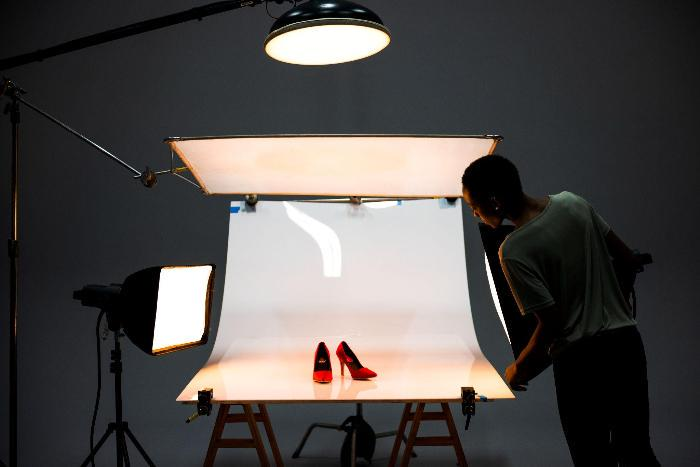 Photographer adjusting light for red high heels, white backdrop