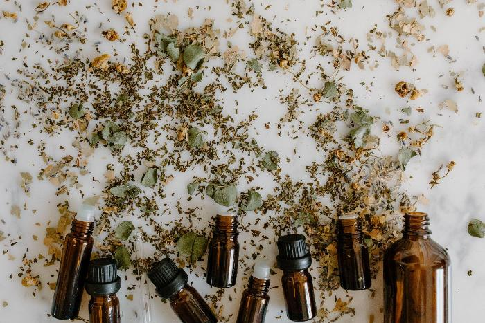 Essential oil bottles among herbs on white flat lay